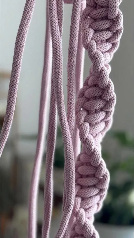 Close-up of hand-knotted macrame cord in soft pink, showing the knots of a wall hanging