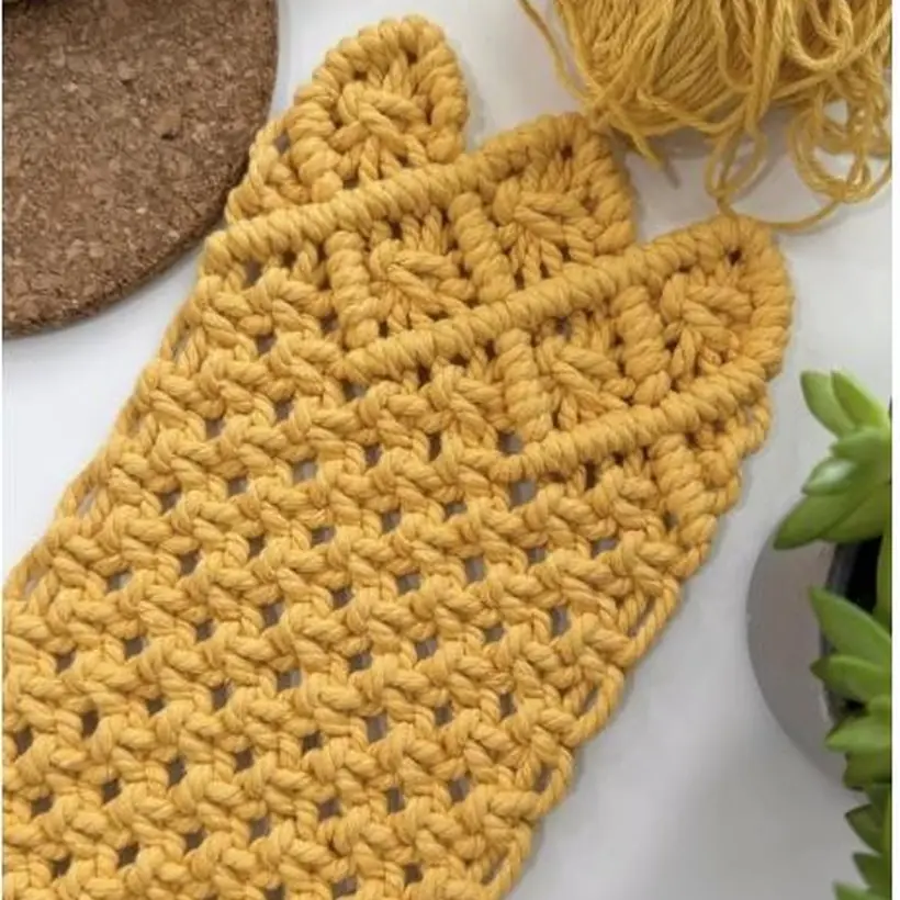 Handmade macrame piece in mustard cotton cord with yarn balls and driftwood, styled flat on white