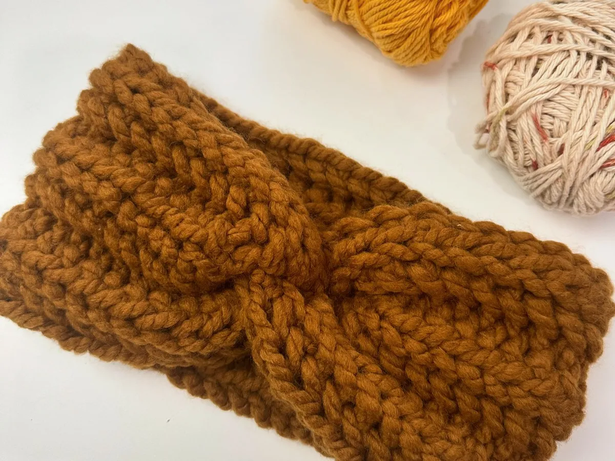 Chunky mustard crochet twist headband beside balls of yarn