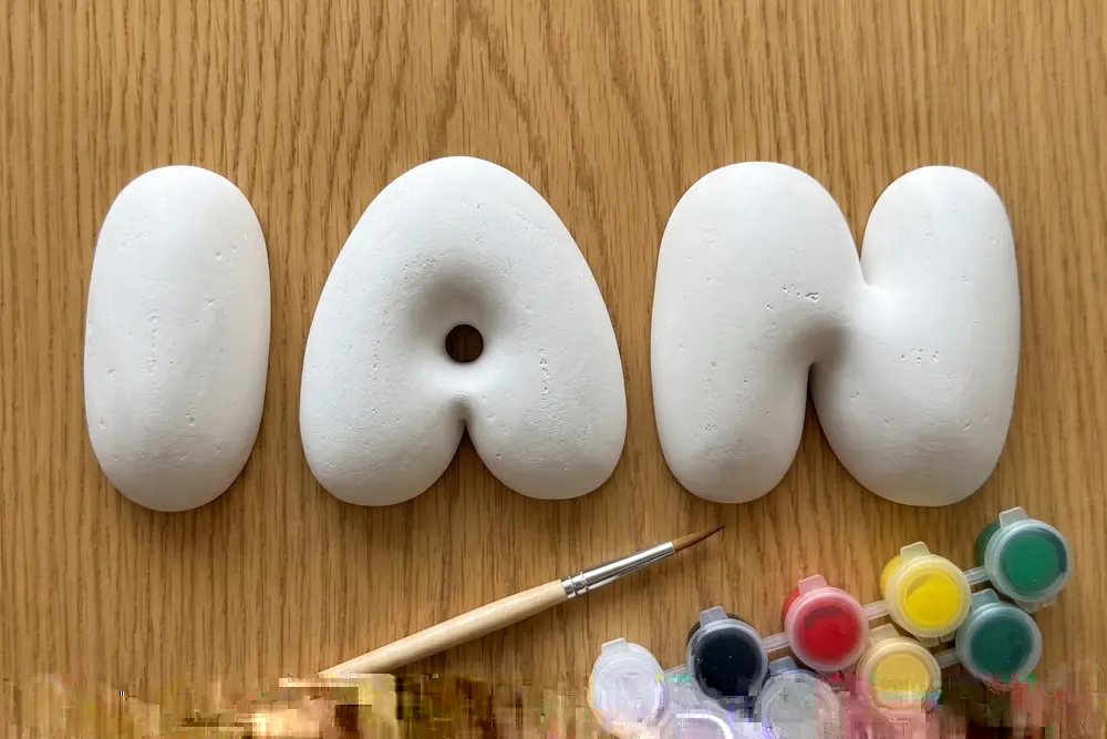 Hand-cast plaster letters spelling the name IAN, with a brush and a set of paints